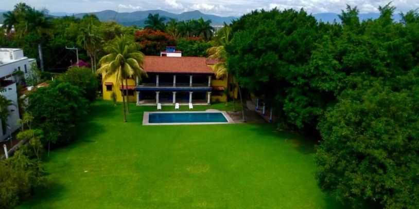 Large house with pool and expansive lawn surrounded by trees.