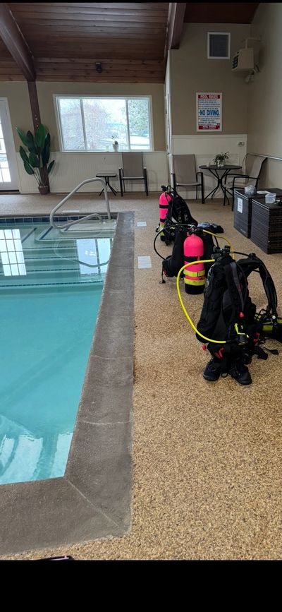 Scuba diving gear lined up beside an indoor pool.