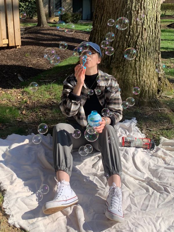 white woman blowing bubbles wearing a plaid shirt and white converse sneakers