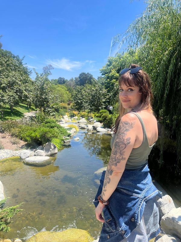 white woman with tattoos and sunglasses standing in front of botanical garden pond 