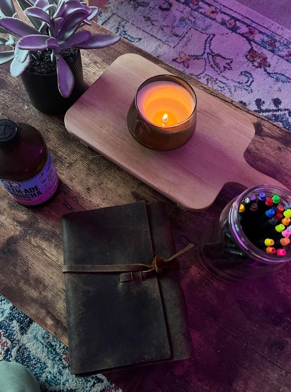 journal and candle on coffee table with plant and kombucha on top of patterned rug