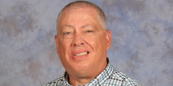 Smiling man in checkered shirt against a neutral backdrop.