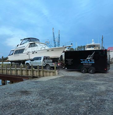 A large boat being transported on a trailer attached to a truck near a dock.