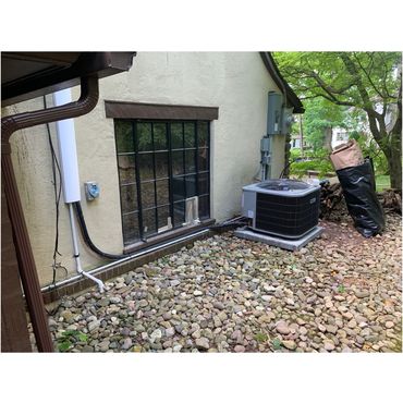Outdoor air conditioning unit installed beside a stone-covered house exterior.