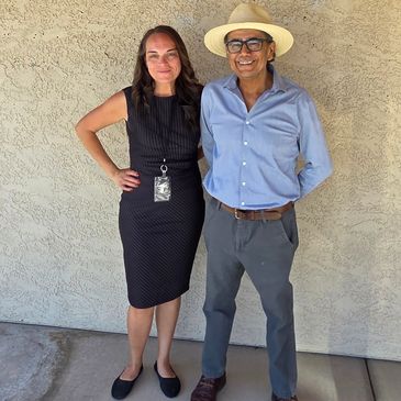 Two people standing side by side against a textured wall, smiling.