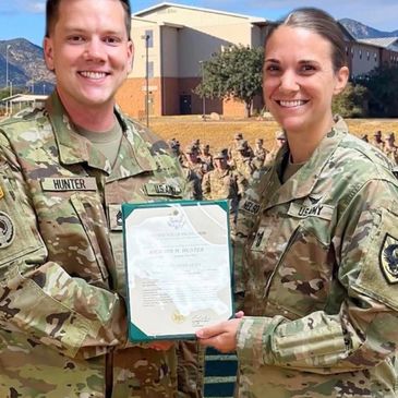 Two U.S. Army soldiers smiling and holding a certificate outdoors.