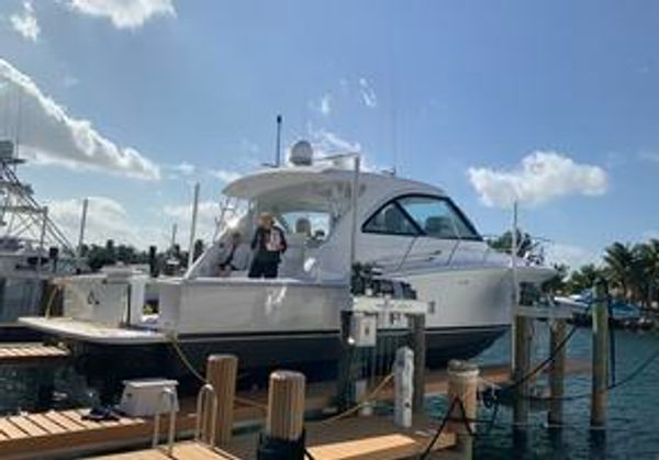 A white yacht docked at a marina with two people on board under a sunny sky.