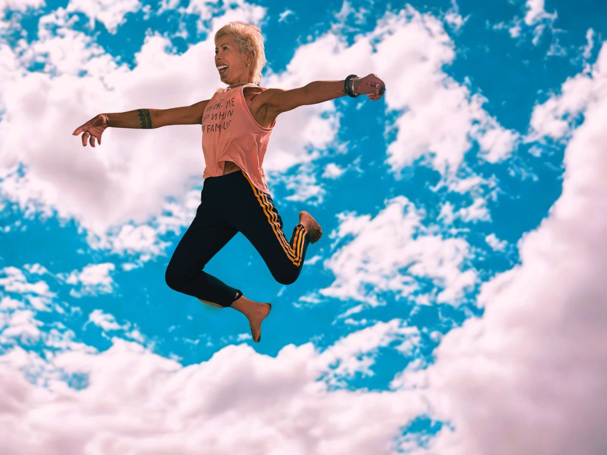 Person joyfully jumping against a bright blue sky with fluffy clouds.