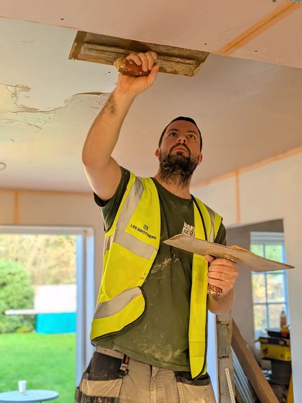 Worker plastering a ceiling wearing a high-visibility vest.