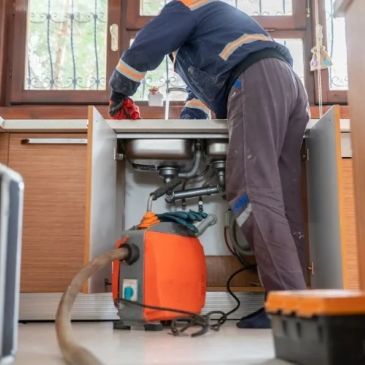 Plumber fixing kitchen sink with tools and vacuum cleaner.