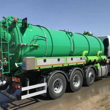 Green vacuum tanker truck parked outdoors on a sunny day.
