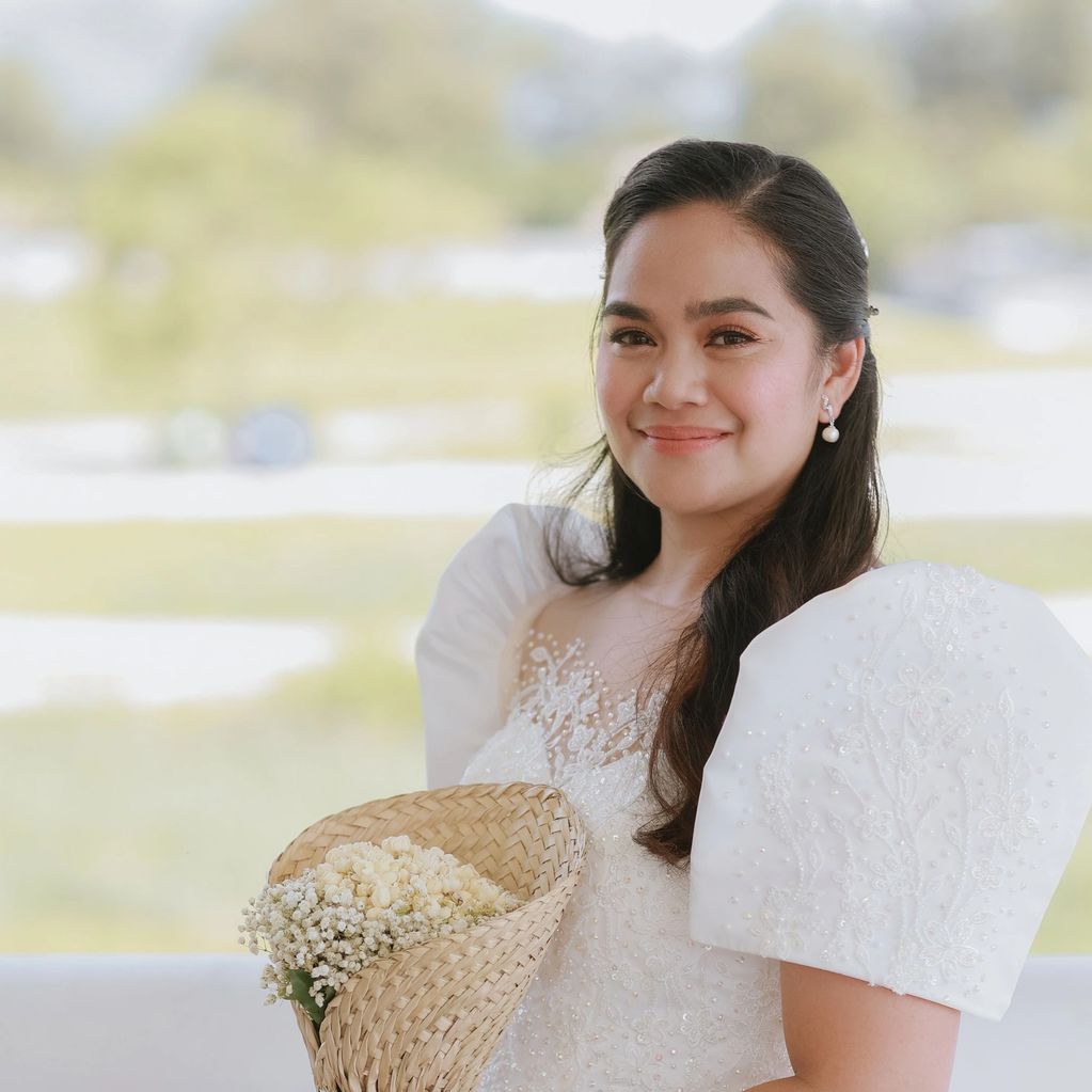 Smiling woman in traditional dress holding a woven basket with flowers.