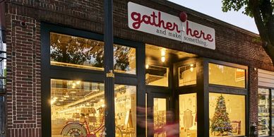 Photo of the gather here storefront at dusk, warm glowing windows featuring hand carved wooden logo 