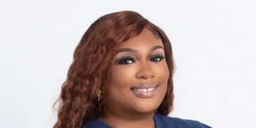 Professional woman with curly brown hair smiling against a white background.