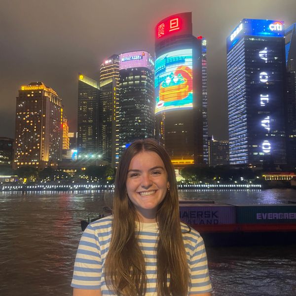 Smiling woman in striped shirt at night with illuminated city skyline behind her.