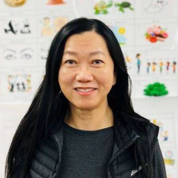 Smiling woman with long black hair standing in front of a wall with drawings.