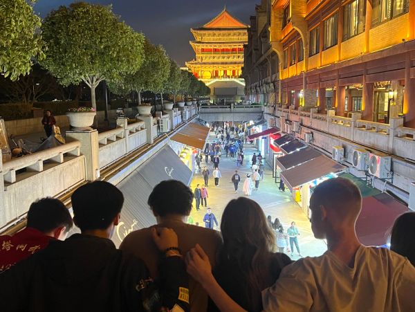 Group of friends enjoying a night view of a bustling, illuminated street and traditional tower.