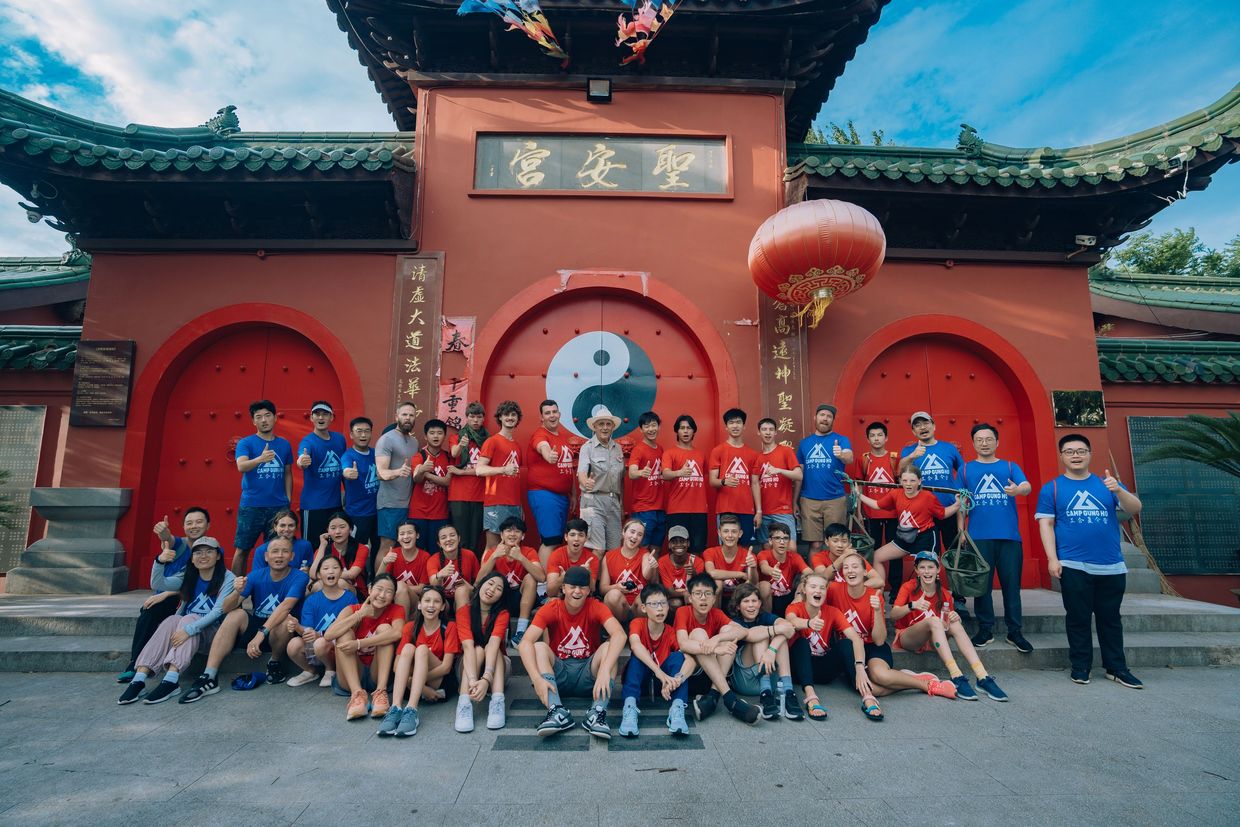 Large group of diverse people posing in front of a traditional Chinese building with a yin-yang symbol.