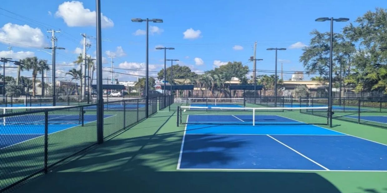 Multiple blue pickleball courts under a clear sky.