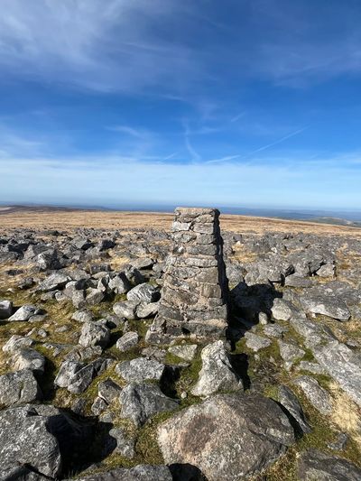 Stone trig point on rocky upland under a clear blue sky.