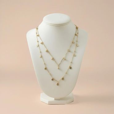 Delicate gold layered necklace with small charms on display bust.