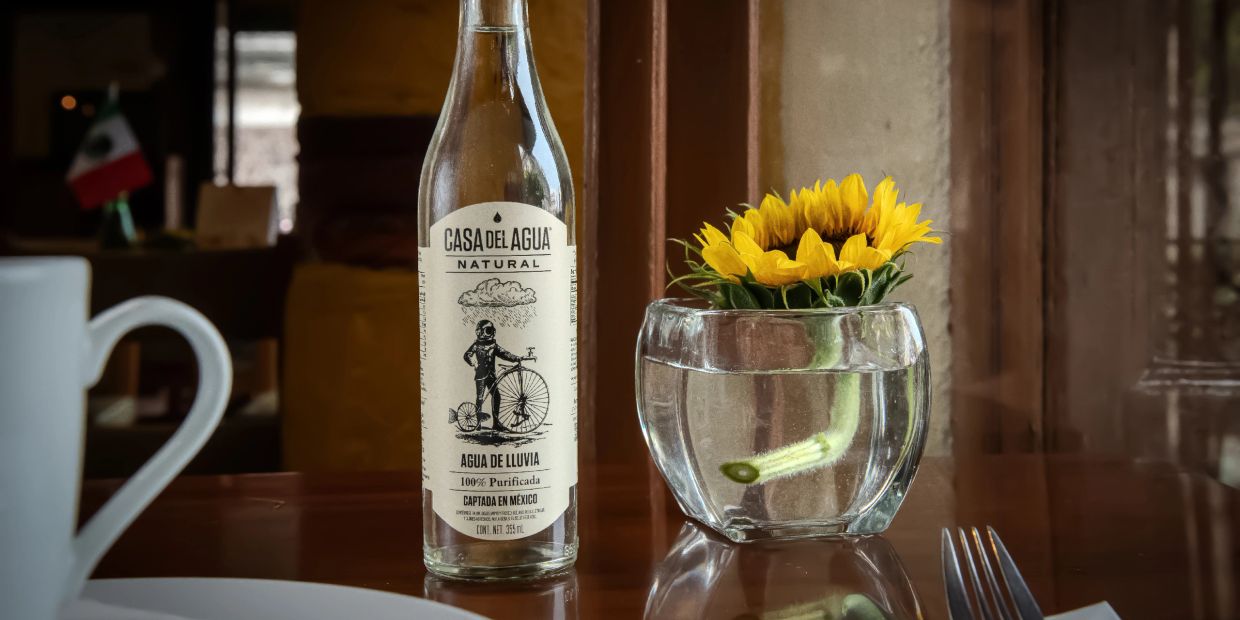 Botella de agua natural y flor amarilla en copa.