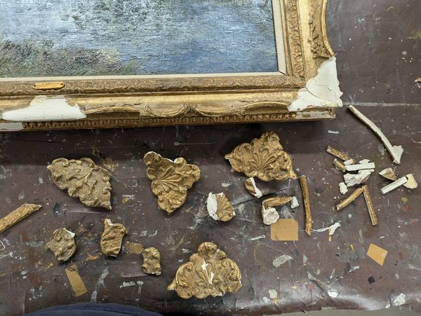 Broken pieces of a decorative gold picture frame on a work surface.