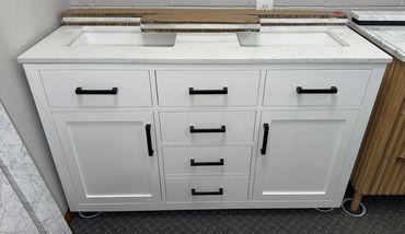 Modern white bathroom vanity with black handles and a dual sink countertop.
