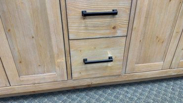 Wooden cabinet with two drawers and black handles on a carpeted floor.