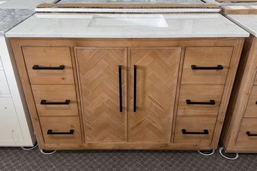 Wooden bathroom vanity with a white marble countertop and black handles.