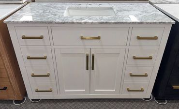 White bathroom vanity with marble top and brass handles.