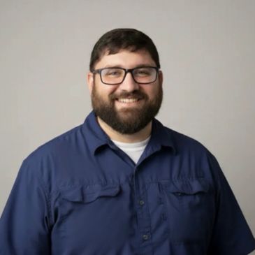 Smiling man with glasses and beard wearing a blue shirt.