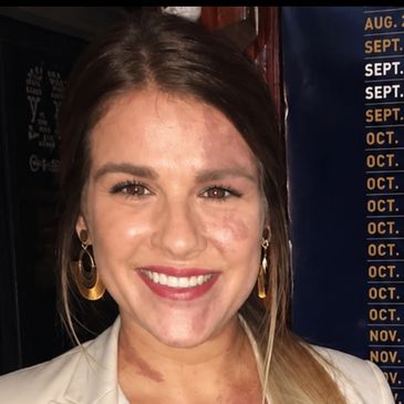 Smiling woman with earrings and light makeup in a casual setting.