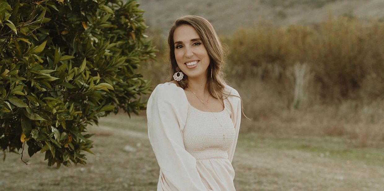 Woman in white dress smiling outdoors.