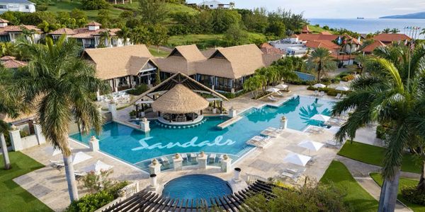 A luxurious tropical resort with a large pool and thatched-roof buildings.