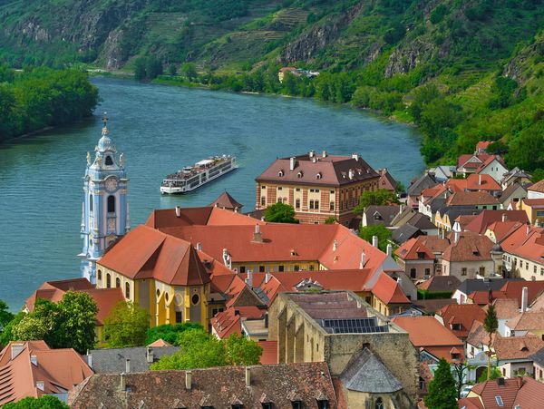 A scenic riverside town with historic buildings and a boat cruising the river.