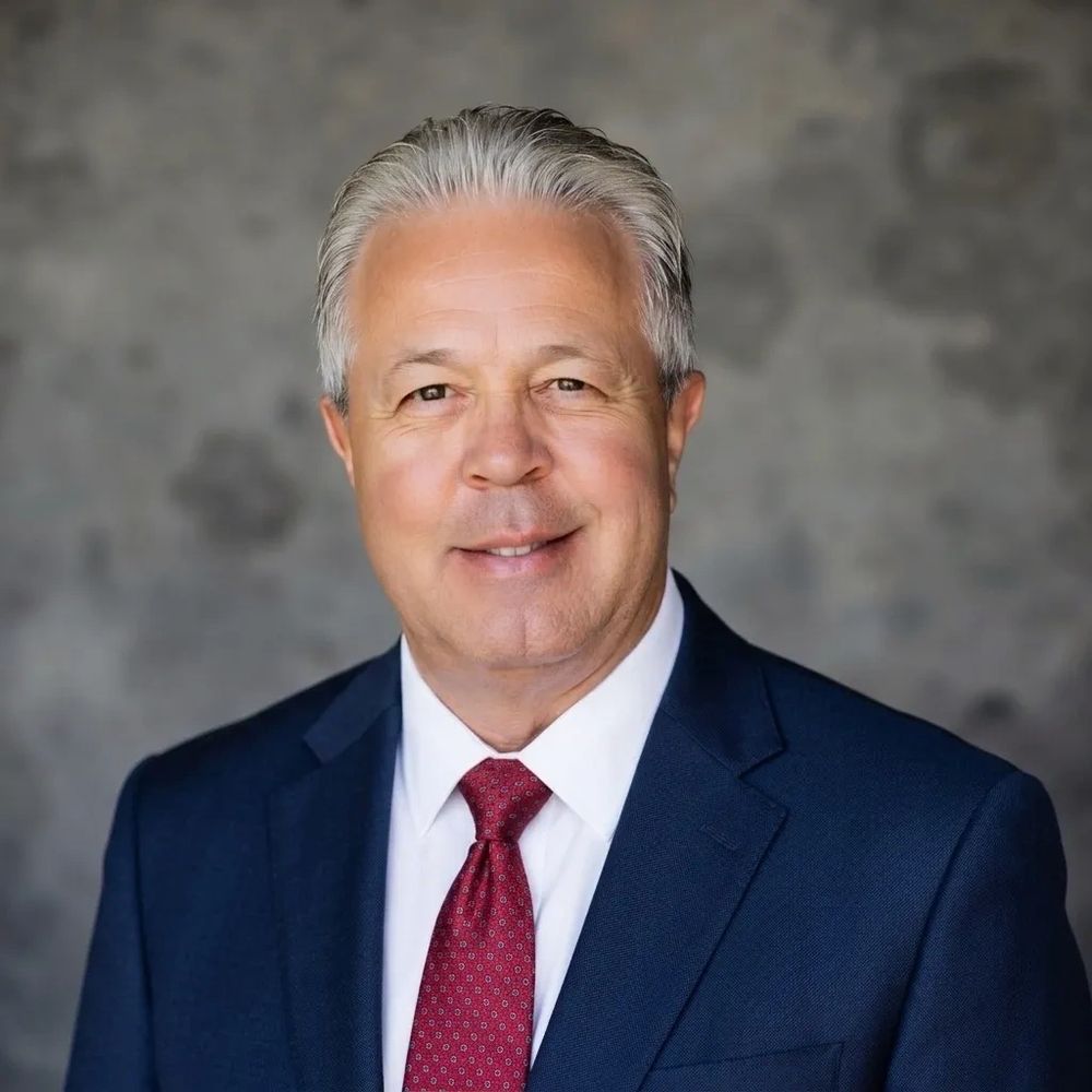 Professional headshot of a smiling middle-aged man in a navy suit and red tie.