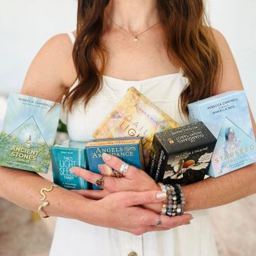 Woman holding six colorful oracle card decks in her arms.