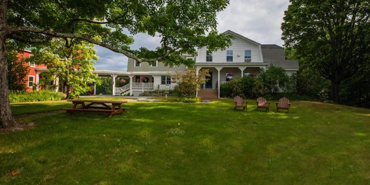 White house with a large green lawn and outdoor chairs.