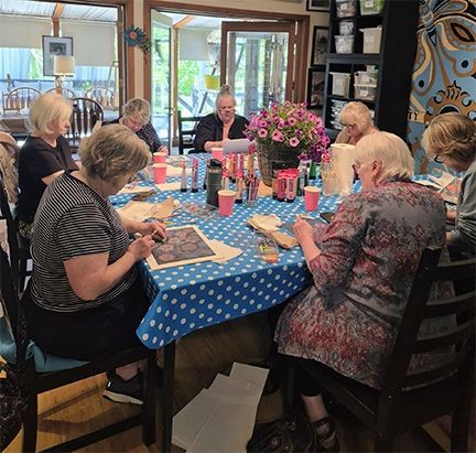 A group of elderly women engaged in arts and crafts around a table.