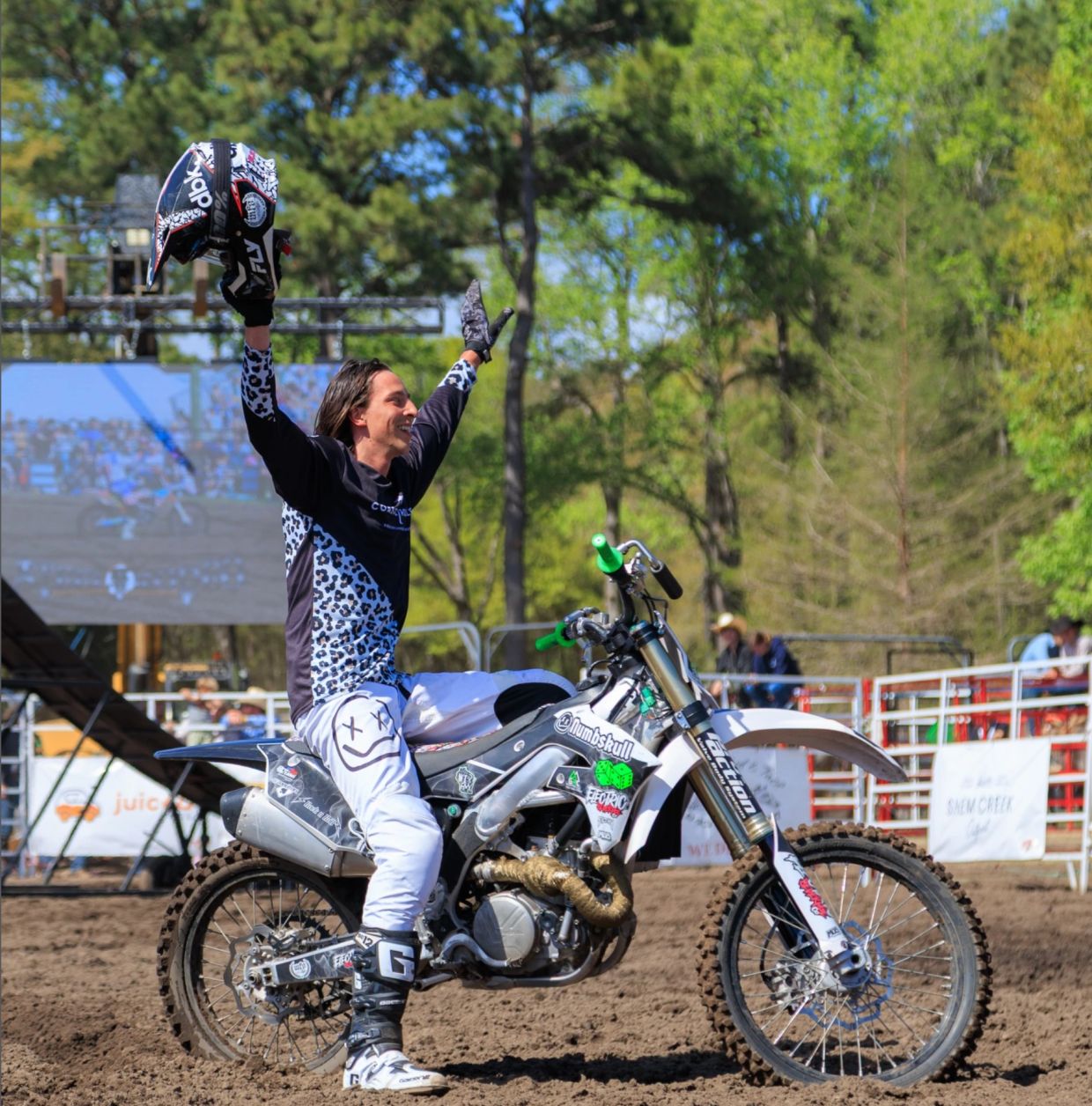 Motorcyclist celebrates with arms raised on dirt bike.