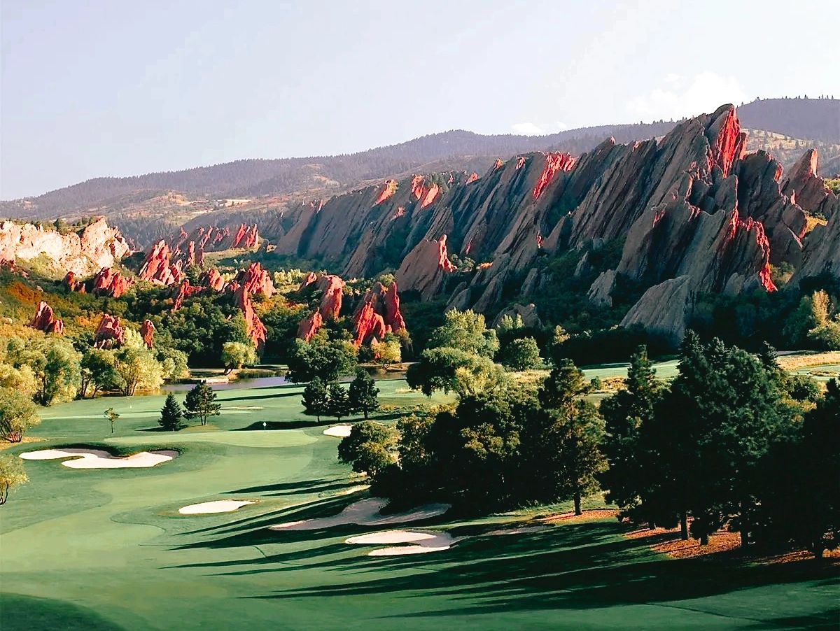 Golf course with red rock formations and green trees in sunlight.