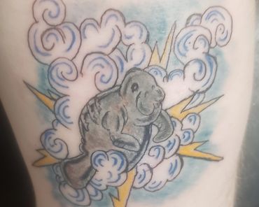 Tattoo of a manatee surrounded by clouds and lightning bolts.