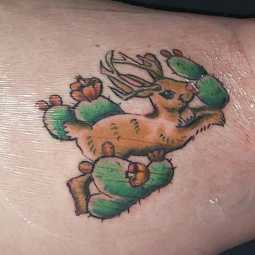 Colorful tattoo of a deer among cacti on skin.