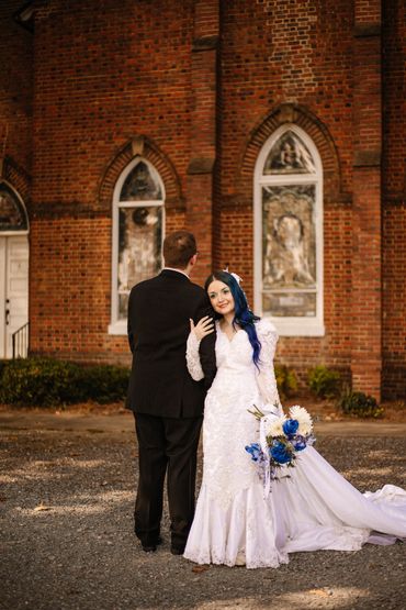 Bride with blue hair and groom pose outside a brick church.