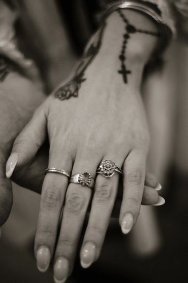 Close-up of a hand adorned with rings and a rosary tattoo on the wrist.