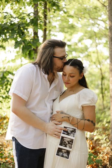 Couple shares a tender moment with ultrasound photos outdoors.