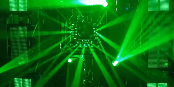 Green laser beams radiate from a central device in a dark setting.
