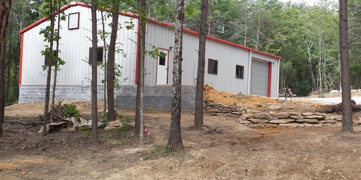 Our woodshop nearing the completion of construction.
Red trim on gray siding in a wooded setting.