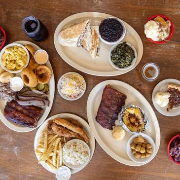 Variety of BBQ dishes with sides and desserts on a wooden table.